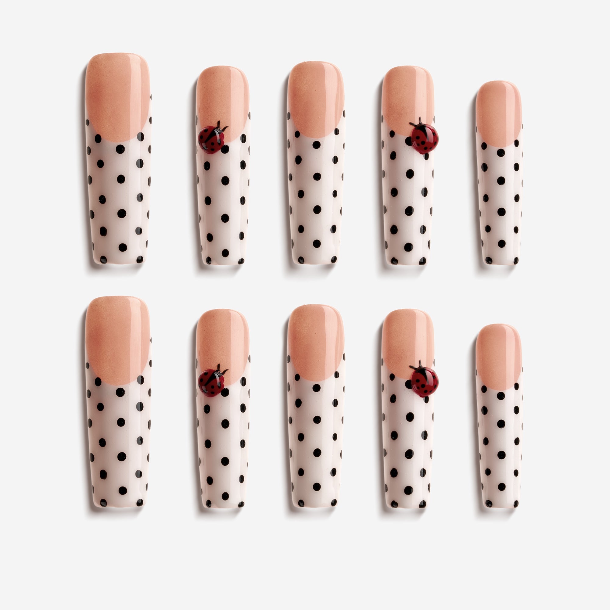 Long press on nails with black polka dots and 3D ladybug charm over nude-white gradient.