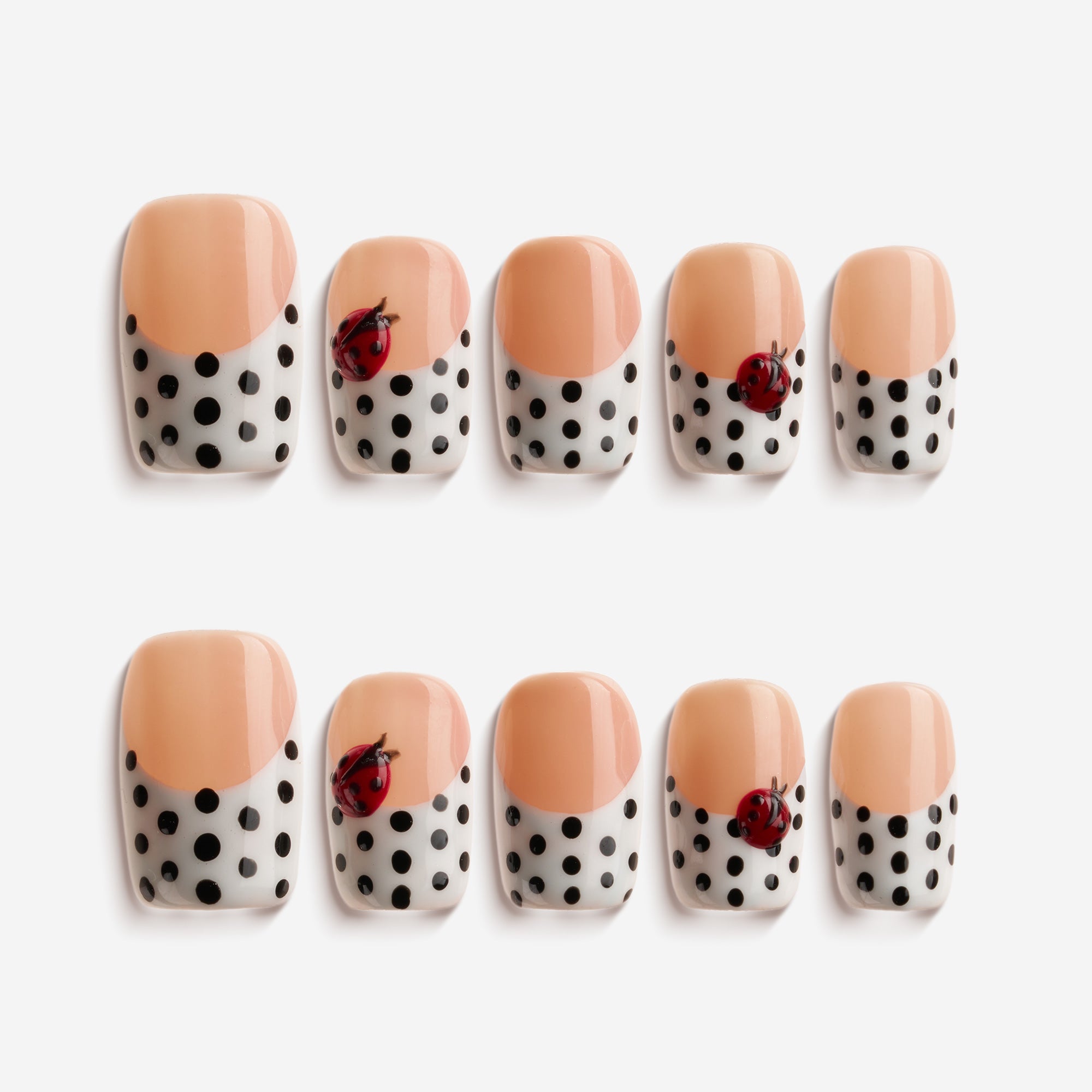 Short press on nails with black polka dots and 3D ladybug charm on nude-white base.