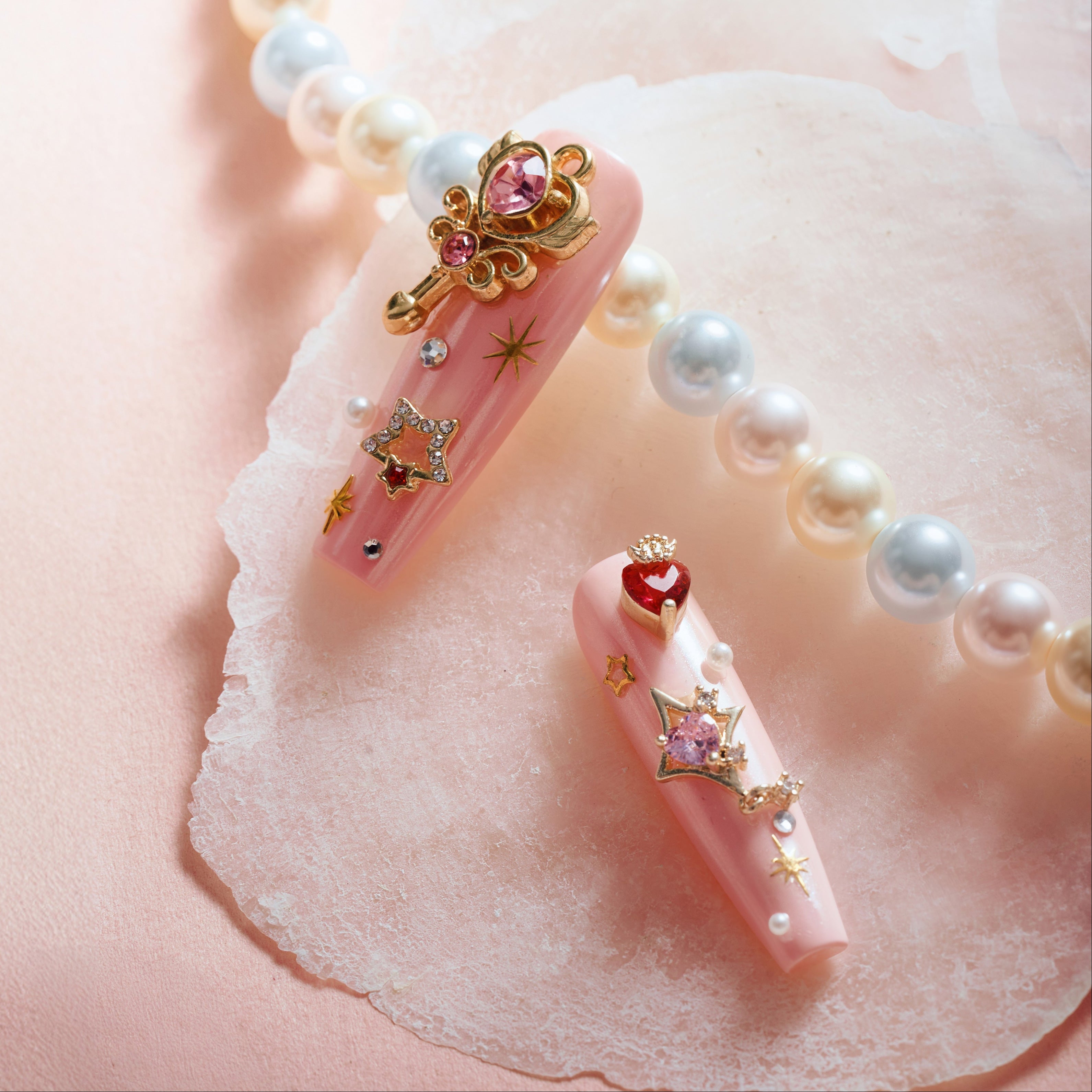 Princess Secret press on nails with gold charms, red gems, pearls, and glossy nude-pink base.