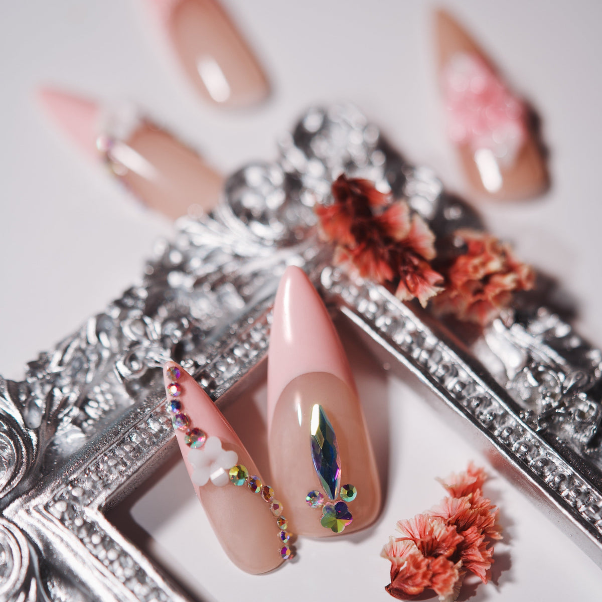 Nude press on nails with silver rhinestone arcs and floral accents. Elegant sparkle and reusable.