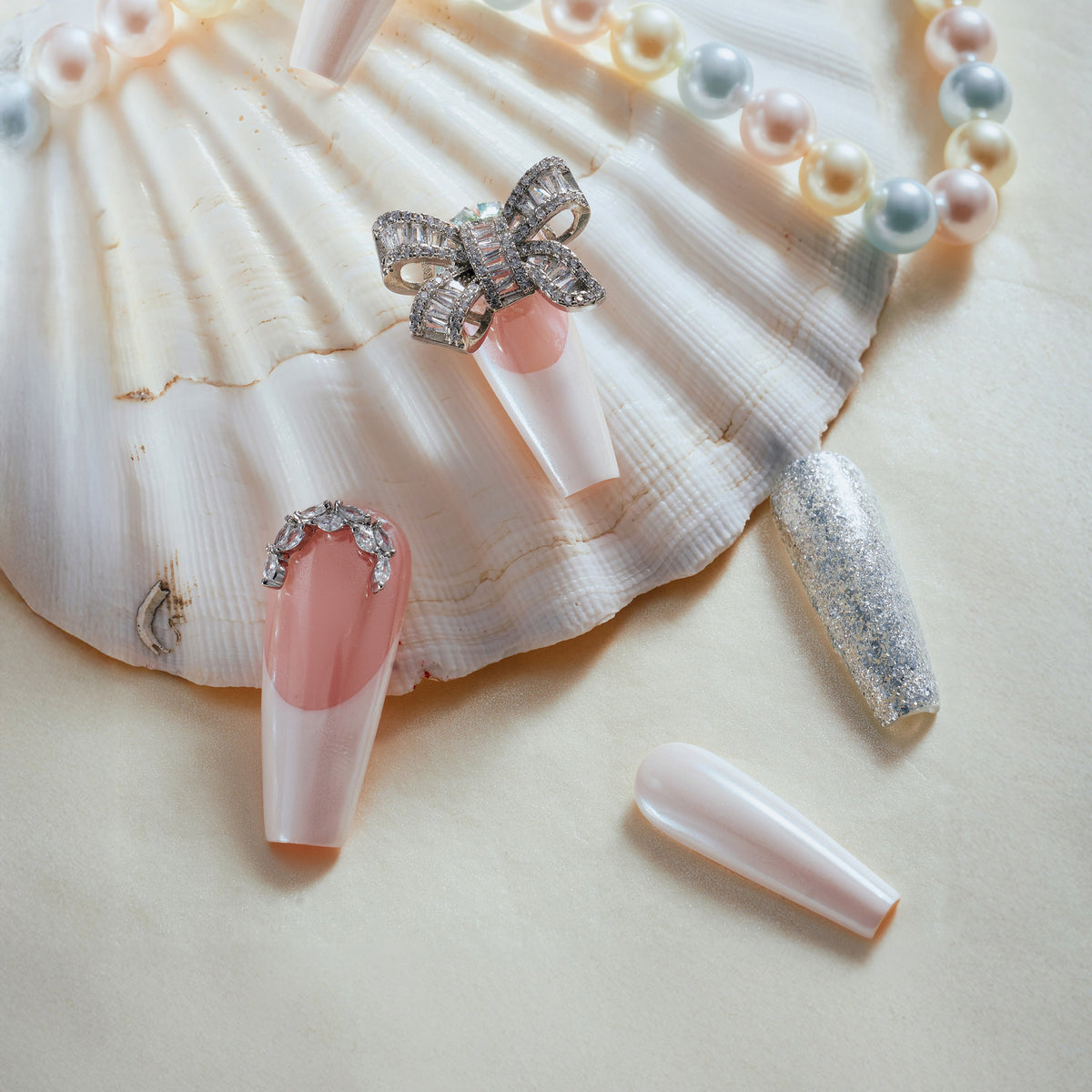 Pink and nude press on nails with silver glitter, rhinestones, and crystal bow charm